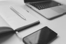 greyscale shot of a laptop, notebook and smartphone