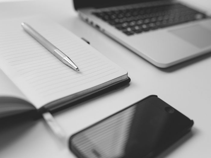 greyscale shot of a laptop, notebook and smartphone