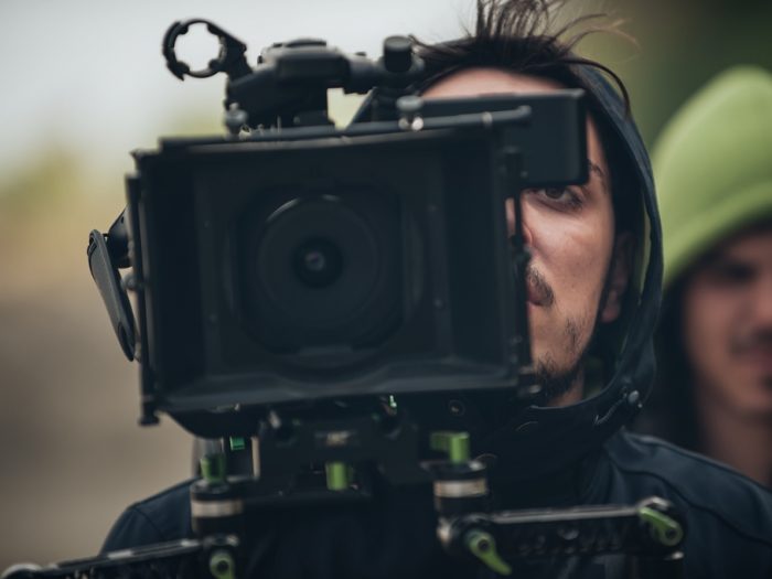 Man using film camera. Another man in green hood in background