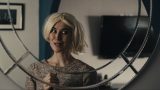 Woman with blonde wig on looking at reflection in a mirror